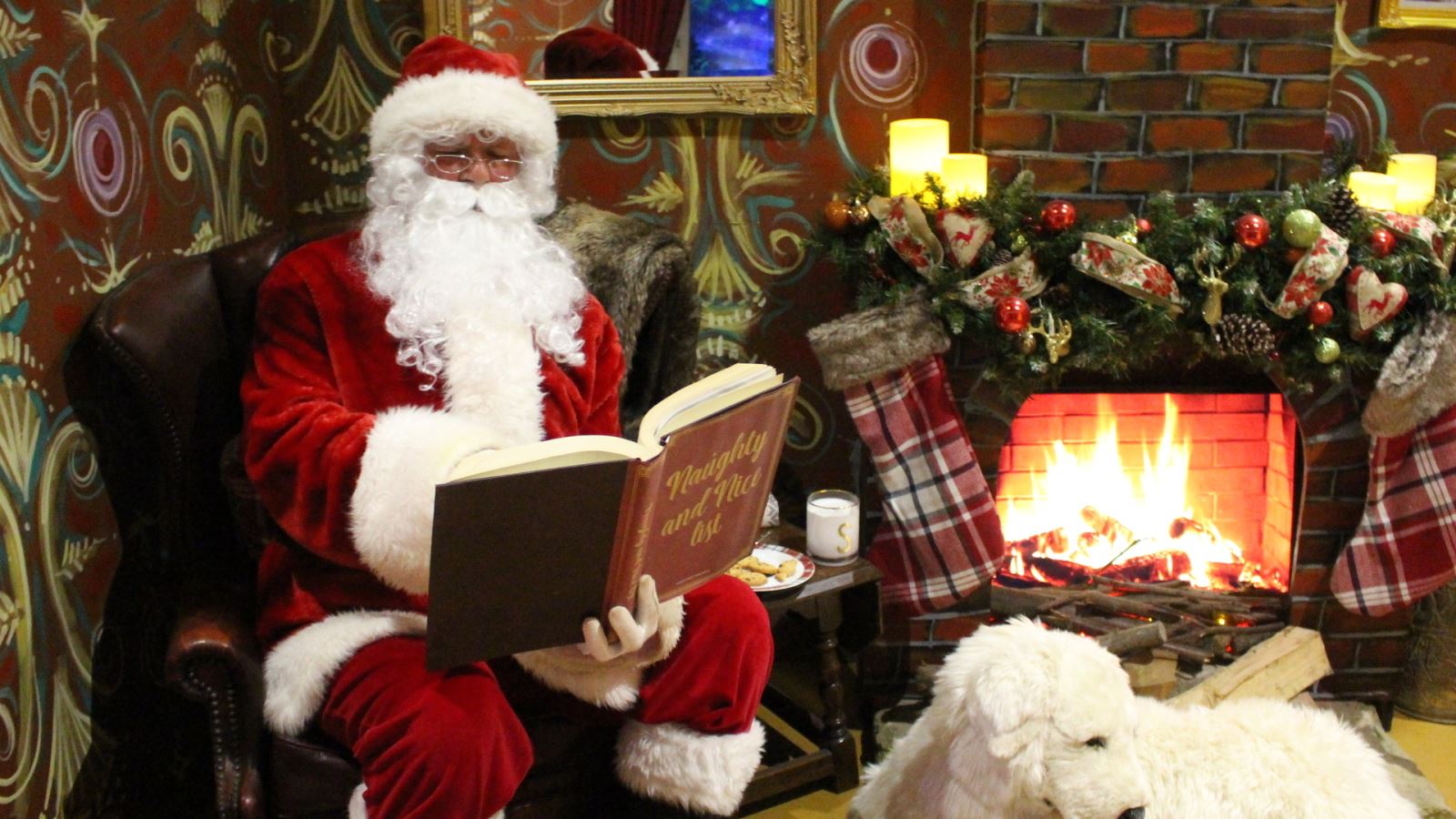 Santa Claus reading a book next to a fireplace
